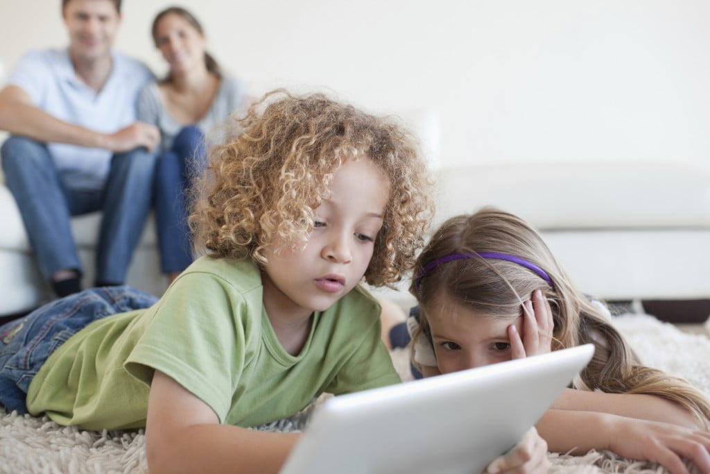 Young children using a tablet computer while their happy parents